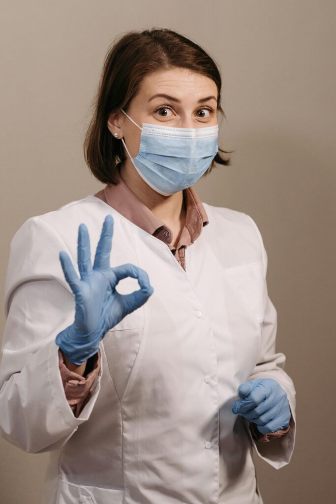 pexels-photo-5998502-5998502 A healthcare worker in PPE showing the OK hand gesture, a sign of assurance.